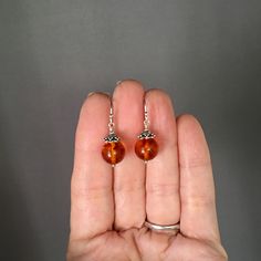 "Gorgeous round Baltic Amber beads are wire wrapped with balled silver pins and topped with Bali Silver caps. These dangle from balled silver earwires. These interesting natural stones feature colors in various shades of orange. Perfect everyday earrings. Each pair of beads will vary. Baltic Amber beads: 10mm Total length of earrings: 1 1/8\" All silver is sterling. As the owner, maker, designer, and curator of this shop, I take great pride in providing you with jewelry that you will love to wea Amber Dangle Earrings With Ear Wire, Amber Czech Glass Dangle Earrings, Amber Beaded Drop Earrings For Gift, Nickel-free Round Sterling Silver Beaded Earrings, Nickel Free Sterling Silver Beaded Earrings, Silver Wire Wrapped Round Bead Earrings, Silver Wire Wrapped Earrings With Round Beads, Gift Sterling Silver Wire Wrapped Beaded Earrings, Handmade Amber Beaded Round Earrings