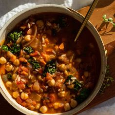 a bowl filled with soup sitting on top of a wooden cutting board next to a spoon