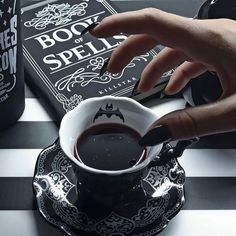 a person is holding a spoon over a cup of coffee on a saucer with a book in the background