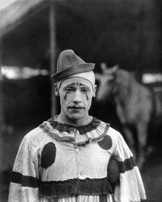 an old black and white photo of a man in clown makeup with a horse behind him