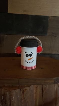 a cup with a snowman face painted on it sitting on top of a wooden table