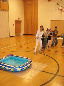 some kids are playing with an inflatable pool on the floor while others watch