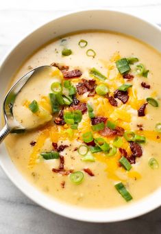 a white bowl filled with soup and topped with bacon, cheese, green onions and jalapenos