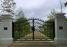 an iron gate in front of a white building with a clock on the wall and trees behind it