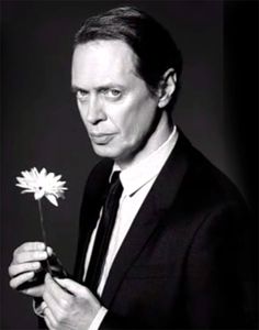 a man in a suit holding a flower and looking at the camera with an intense look on his face