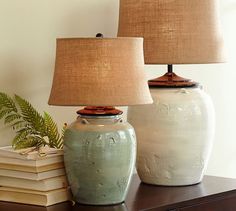 two ceramic vases sitting on top of a table next to a lamp and books