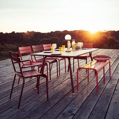 an outdoor table and chairs on a wooden deck with the sun setting in the background