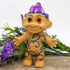 a small figurine is standing next to some purple flowers