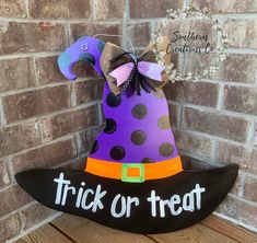 a trick or treat hat sitting on top of a wooden sign next to a brick wall