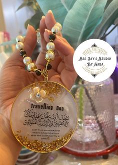 a person holding up a necklace with gold and white beads on it, in front of a potted plant