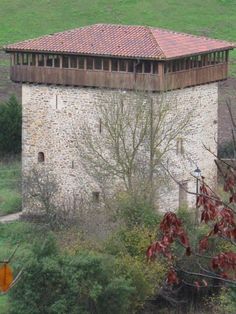 an old brick building in the middle of a green field with trees and bushes around it