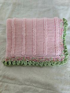 a pink and green crocheted blanket laying on top of a white bed sheet