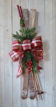 a christmas wreath made out of wood sticks and holly with two shovels hanging on the wall