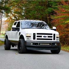 a white pickup truck parked on the side of a road in front of some trees