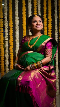 a woman in a green and pink sari sitting on a chair with flowers behind her