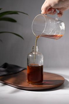 a person pours syrup into a glass bottle on a wooden tray next to a potted plant