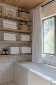 a bathtub with lots of white towels on the shelves next to it and a window