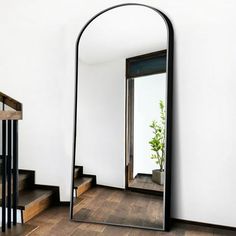 a mirror sitting on top of a wooden floor next to a stair case with a plant in it