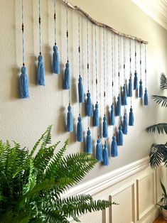 a wall hanging with blue tassels on it next to a potted plant