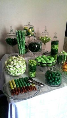 a table topped with lots of candy and green candies on top of it's trays