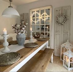 a wooden table topped with plates and vases filled with flowers next to a window