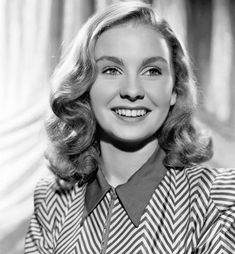 a black and white photo of a woman with blonde hair wearing a striped shirt smiling at the camera