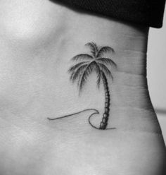 a small palm tree tattoo on the back of a woman's stomach, with a wave coming up from it