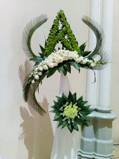 a white vase with green and white flowers in it sitting on a table next to a pillar