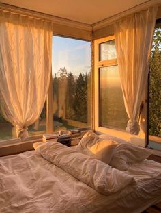 an unmade bed sitting in front of two windows with curtains on each window sill