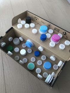 an open cardboard box filled with lots of different colored cups and lids on top of a wooden floor