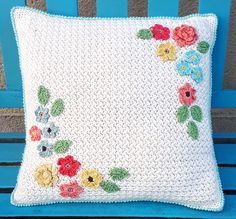 a crocheted pillow with flowers on it sitting on a blue bench in front of a wall