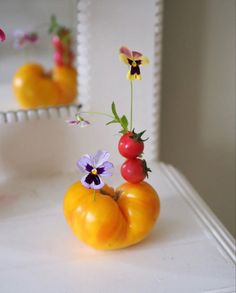 two small vases filled with different types of flowers and fruit sitting on a table