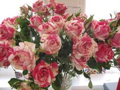 a vase filled with pink and white flowers on top of a counter next to a window