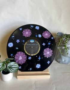 a record sitting on top of a wooden stand next to a potted plant and vase