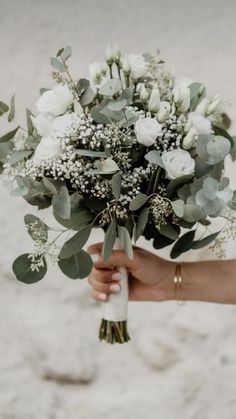 a person holding a bouquet of flowers and greenery in their hand on the beach