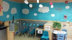 a classroom with blue chairs and white clouds on the wall above it is a small desk