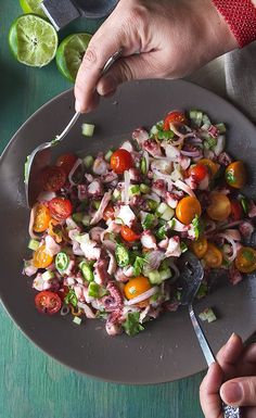 a person is holding a spoon over a plate of food that includes tomatoes, onions and cucumbers