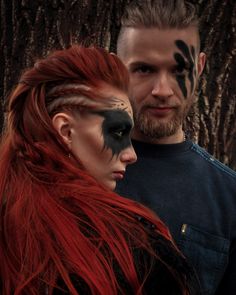 a man and woman with face paint standing next to each other in front of a tree