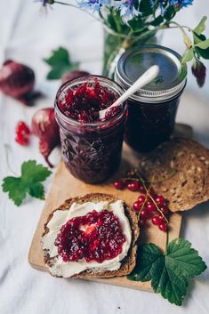 two jars of jam sit on a cutting board next to some bread and berries, with flowers in the background