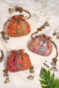 three small purses with tasseled handles on a white surface next to a plant