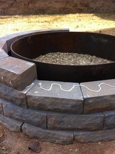 an outdoor fire pit with rocks around it and wires running through the top, along with gravel