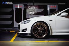 a white car parked in a parking lot next to a wall with two machines behind it