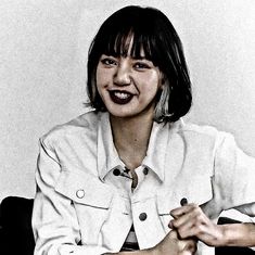 a black and white photo of a woman sitting in a chair smiling at the camera