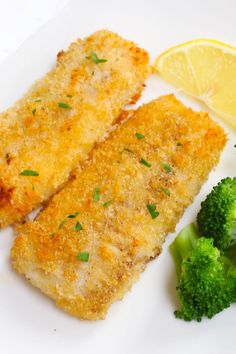 two pieces of fish and broccoli on a white plate with lemon wedges