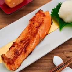 a piece of salmon on a white plate with chopsticks