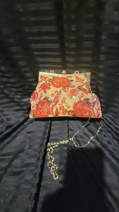 an orange and yellow purse sitting on top of a black cloth covered table next to a chain