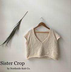 a knitted crop top is hanging on a hanger next to a dried plant