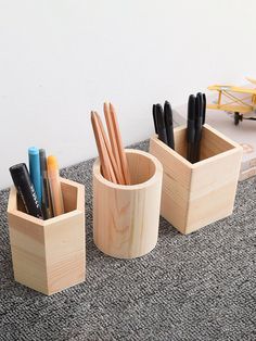 three wooden containers with pens and pencils in them sitting on the floor next to a toy airplane