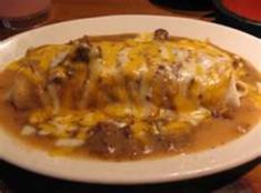 a white plate topped with meat and cheese covered in gravy on top of a wooden table