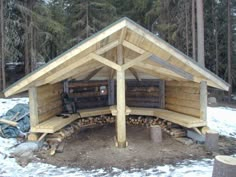 a small wooden shelter in the middle of some snow covered ground with logs stacked around it